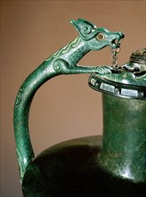 Handle of a bronze jug inlaid with coral and enamel in the form of an animal head