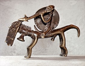 A brass weight for weighing gold dust in the form of a horse and rider carrying a spear and shield