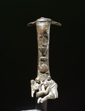 Bronze handle from an oinochoe, decorated in relief with scene of two dwarves boxing or wrestling, watched by an umpire