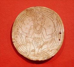 Shell gorget depicting a flying shaman with a deaths head in one hand and a ceremonial mace in the other