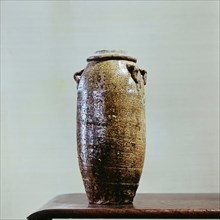 A tall thin vase with a lid, coated with a black glaze