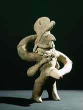 Standing ithyphallic figure, with hat and necklace, holding phallus