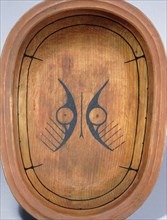 Wooden serving dish with stylized animal face decoration based on nucleated circle eyes
