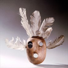 A mask of wood and feathers which bears a black eye, perhaps a humorous detail to the shaman who carved it