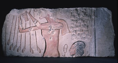 Sunk relief of Akhenaten offering a bouquet to Aten while behind him his daughter with her hair arranged in the side lock of youth rattles her sistum