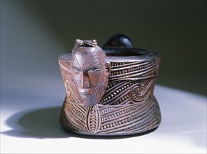 A oval lidded wooden box with scrolled carvings on the sides and a male and female head carved at the ends