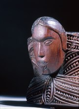 A oval lidded wooden box with scrolled carvings on the sides and a male and female head carved at the ends