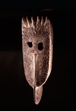 A wooden face mask with remnants of red seeds attached