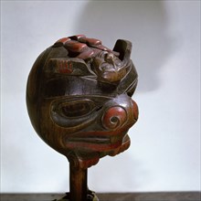 Shamans rattle carved in the form of a head with a humanoid figure lying across the top