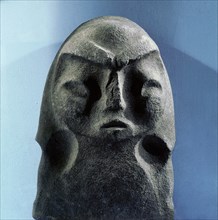 Stone pile driver with a human head carved on one side