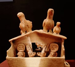 Model of a house with people drinking and birds sitting on the roof