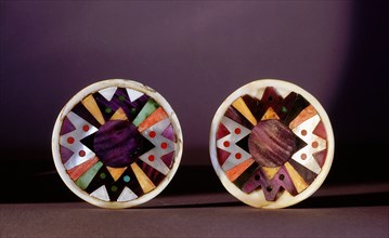 Two discs of turquoise and shell (and possibly jet and lapis), with an abstract geometric design, used either as earrings or worn on clothing