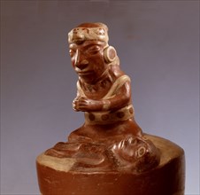 In typically Mochica style, this modelled ceramic shows a priest or shaman engaged in a curing ritual or praying over a deceased person