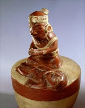 In typically Mochica style, this modelled ceramic shows a priest or shaman engaged in a curing ritual or praying over a deceased person