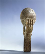 Wooden hand holds a disc on which are carved mythological scenes