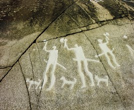 Petroglyph with three men brandishing axes, accompanied by dogs
