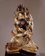 Vajrasattva, also known as Vajradhara, the Supreme Buddha, identified by his hands which are held in the Vajrahumkara mudra, a thunderbolt in each, sits in yab yum with the Supreme Wisdom Visvatara