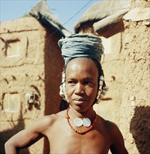 A Dogon woman, her hair plaited through a shell ornament, wearing a turban and jewellery