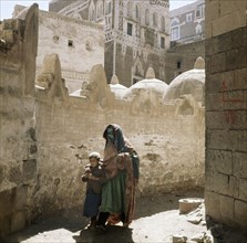 Veiled woman with a child in the street, San'a