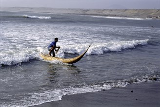 Modern day Moche fisherman guiding a tortora reed boat (caballito) on beach on Peru's northern coast