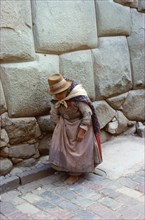 Quechua (Inca) woman in Colonial-period dress walking past typical Inca Masonry in the famous Inca Street of Hatun Rumiyoc, Cuzco