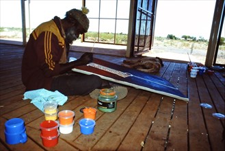 Desert artist Flakky Stevens painting on the verandah at the Warlayirti Culture Centre in the north-west desert region of Western Australia south of Halls Creek