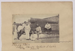 Group of men in civilian clothes pose by cannon