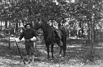 A member of the cavalry poses standing in front of his horse