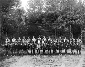 A group of fourteen men on horses pose for a group portrait.