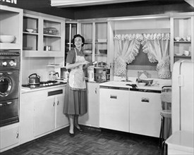 United States: c. 1950. 
A woman wearing an apron in the kitchen of a model home making a sandwich