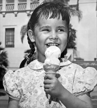 California:  c. 1948.
A smiling young ethnic girl in pigtails enjoys eating a double dip ice cream