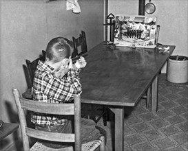 United States:  c. 1950.
A boy shoots at a birds on a wire game with a cork gun on the family table