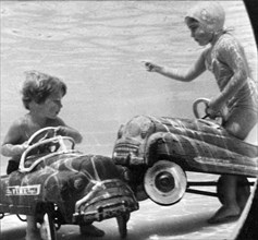United States:  c. 1958.
Two children move their playground toys into the pool, where accidents are
