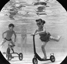 United States:  c. 1958.
A group of children move their playground toys into the pool.