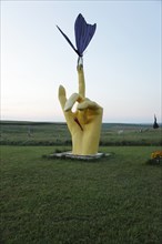 Hand with finger extended holds a butterfly; Located just off Interstate 90 in the South Dakota Drift Prairie, about 25 miles west of Sioux Falls. Many of the sculptures, in the style of industrial ar...