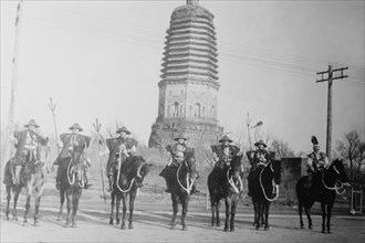 7 Chinese Gendarmes in peaked hats are mounted as skirmishes as cavalry in front of a temple.