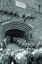 71st Street Armory in New York welcomes uniformed doughboys in formation with rifles and full pack; a sign above the portcullis of the emulated stone castle invites men to enlist to fight in World War...