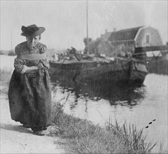 A Older Dutch woman has a bustle around her chest as she pulls a barge down a canal.