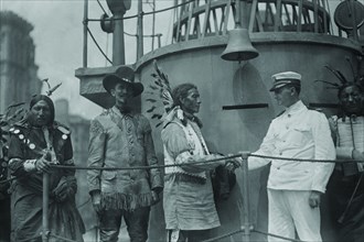 A War Bonneted Native American shakes hands with the Commander of the "Recruit", a facsimile Battleship constructed in the center of Manhattan to aid in enlisting men to fight in Europe in WWI;  1917