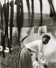Black and white, an informal portrait of a young Black woman surrounded by laundry in Newport, R.I. 1902