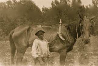 African American boy standing with horse attached to plow 1899