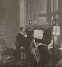 African American Man in suit gives piano lessons to a young white girl 1900