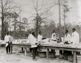African American men preparing to serve a meal in an outdoor setting among trees 1900