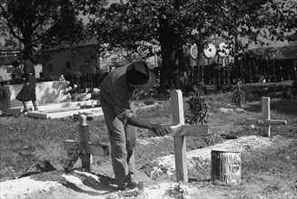 African American paints the crucifix marking a gravesite in a cemetery 1938