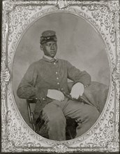 Seated black soldier, frock coat, gloves, kepi 1865