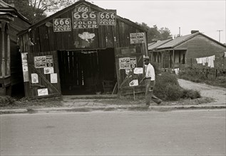 African American walks in front of, Advertisements for popular malaria cure, Natchez, Mississippi 1935