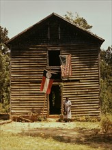 African American woman standing by building with Georgia state and United States flags. 1941