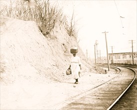 African American woman with basket on head walking near railroad tracks 1921