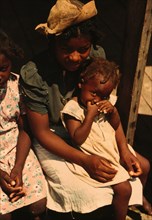 Three Black children sitting on the porch of a house 1940