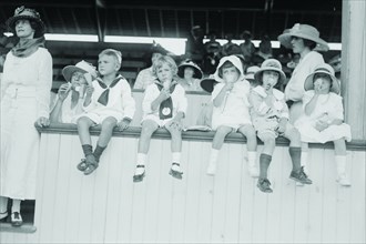 Children sit on wall in front of stands at the ballpark and eat ice cream cones.